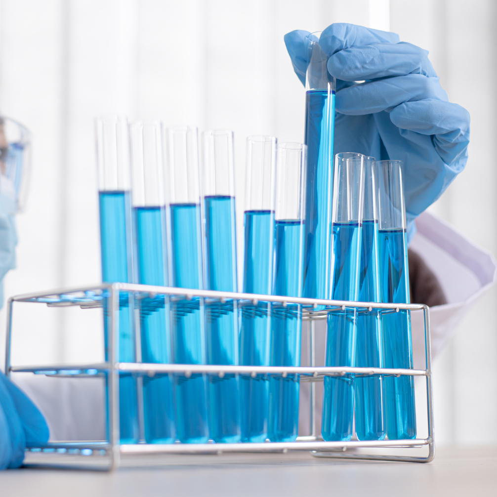 a blue-gloved hand lifting a blue sample in a long test tube from the middle of a full line of tubes 