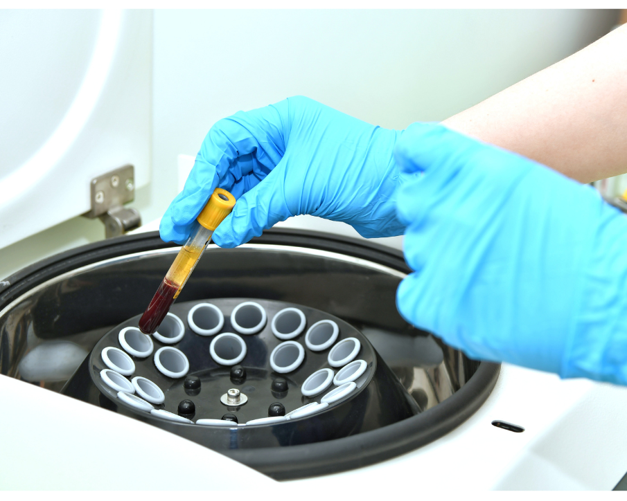 a blue-gloved hand placing a vial into a centrifuge 