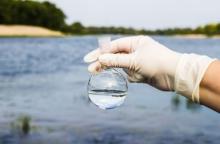 Hand with glove holding round bottom flask full of water in front of lake